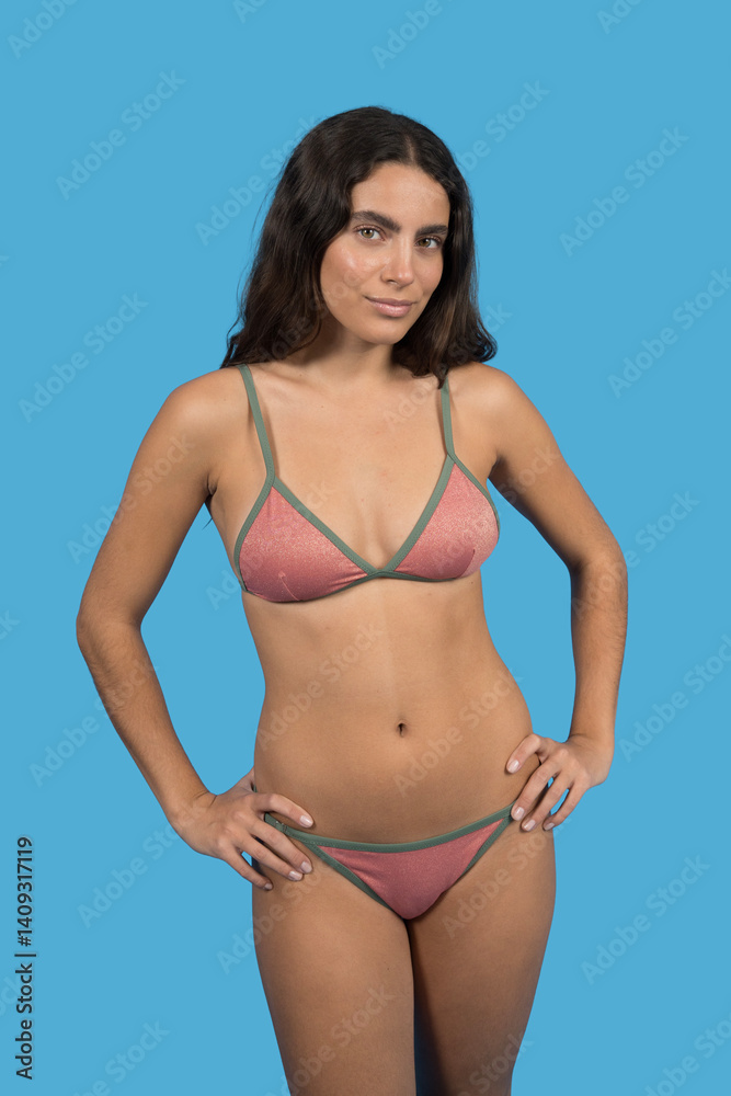 Fototapeta premium Confident model posing in pink and green bikini on blue backdrop