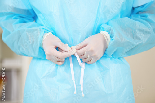 Healthcare professional in blue protective gown tying knot