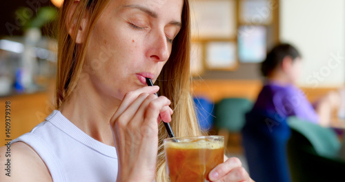 Woman enjoys iced coffee with straw in cozy cafe with blurred background