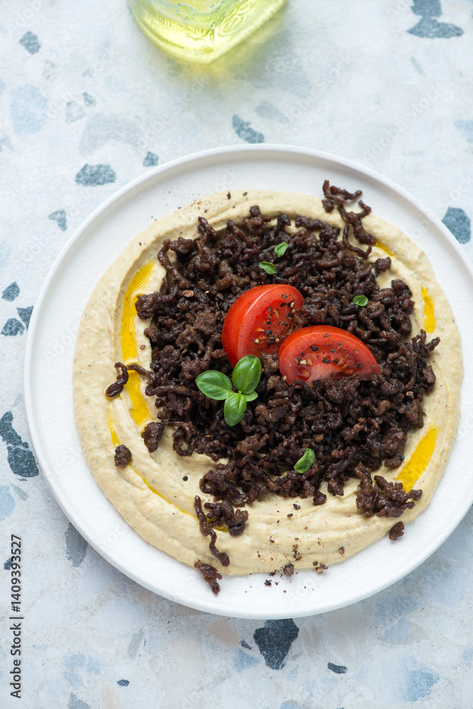 Hummus with roasted ground beef and tomato wedges, vertical shot on a white and blue granite background, high angle view Hummus with roasted ground beef and tomato wedges, vertical shot on a white and blue granite background, high angle view