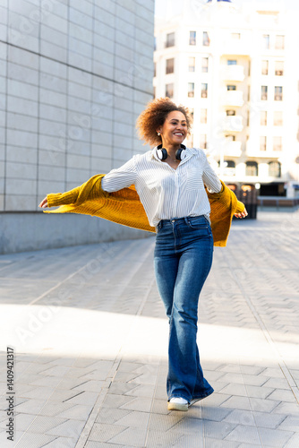 Happy young woman walking in the city wearing headphones and smiling