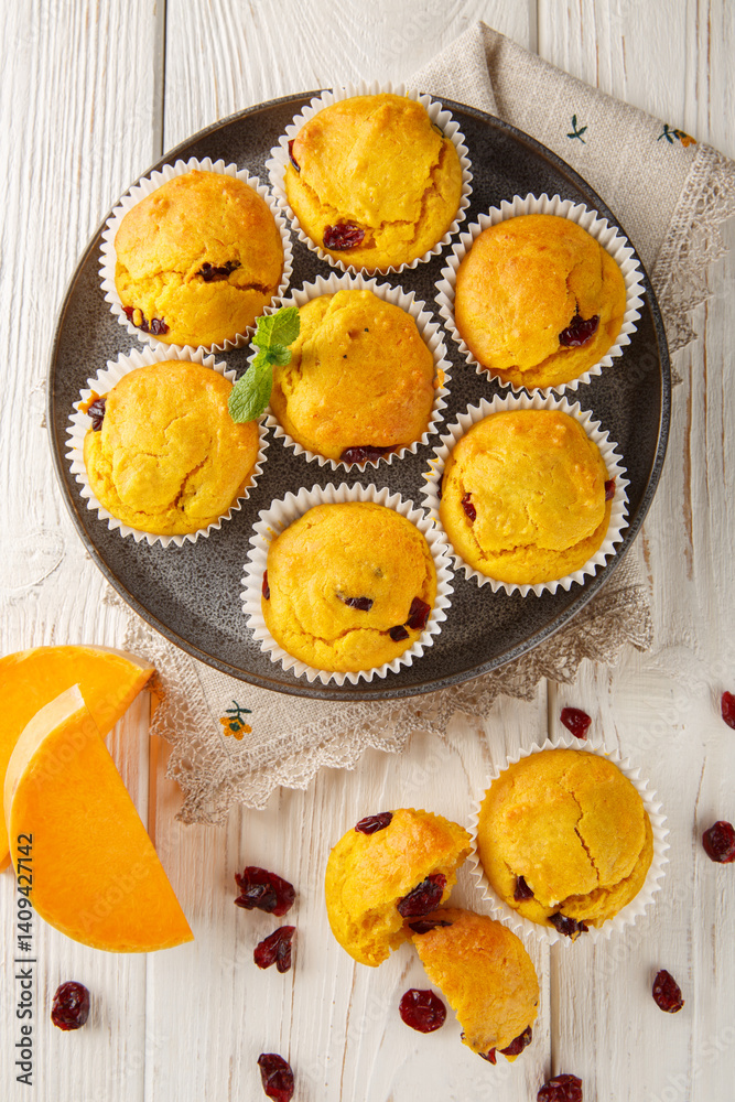 Soft and fluffy muffins flavored with pumpkin, cranberries, warm spices, and a touch of orange closeup on the plate on the wooden table. Vertical top view from above
