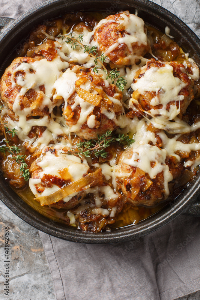 Cheesy French onion meatballs with caramelized onions gravy and gooey cheese closeup on the table. Vertical top view from above