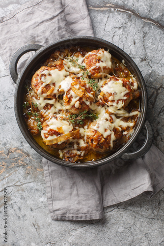 Obraz na płótnie French onion meatballs are nestled into a rich, savory onion sauce and topped with Gruyere and mozzarella cheese closeup on the pan on the table. Vertical top view from above w salonie