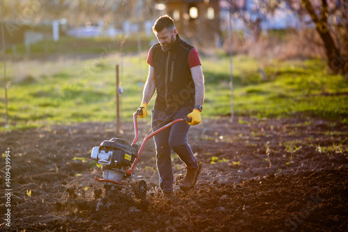 organic farming man ploughs the ground at sunset with a tiller preparing the soil for sowing