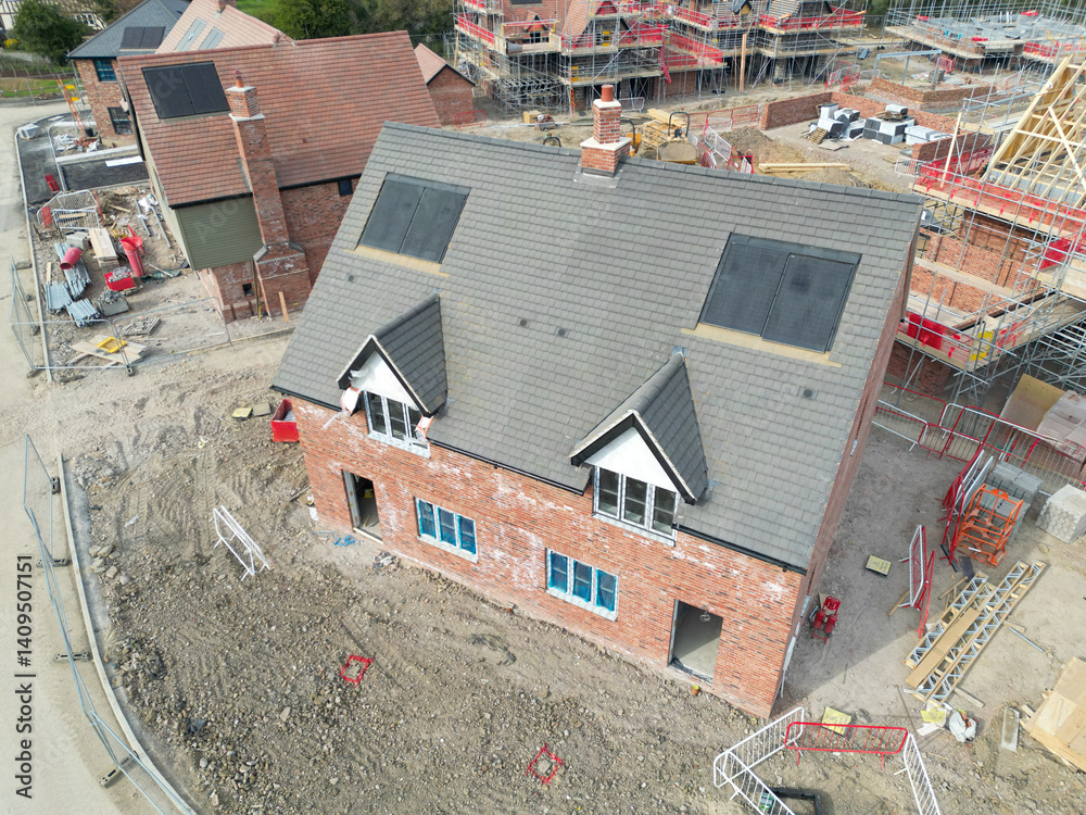 Near completed semi detached homes seen on a busy housing development site in rural Britain. Larger, detached homes can be seen in the background.