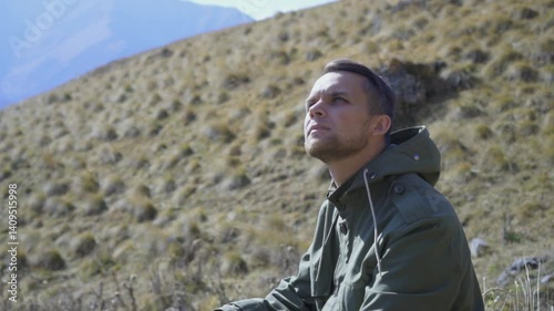 A traveler with a backpack rests and admires the view against the background of the mountains