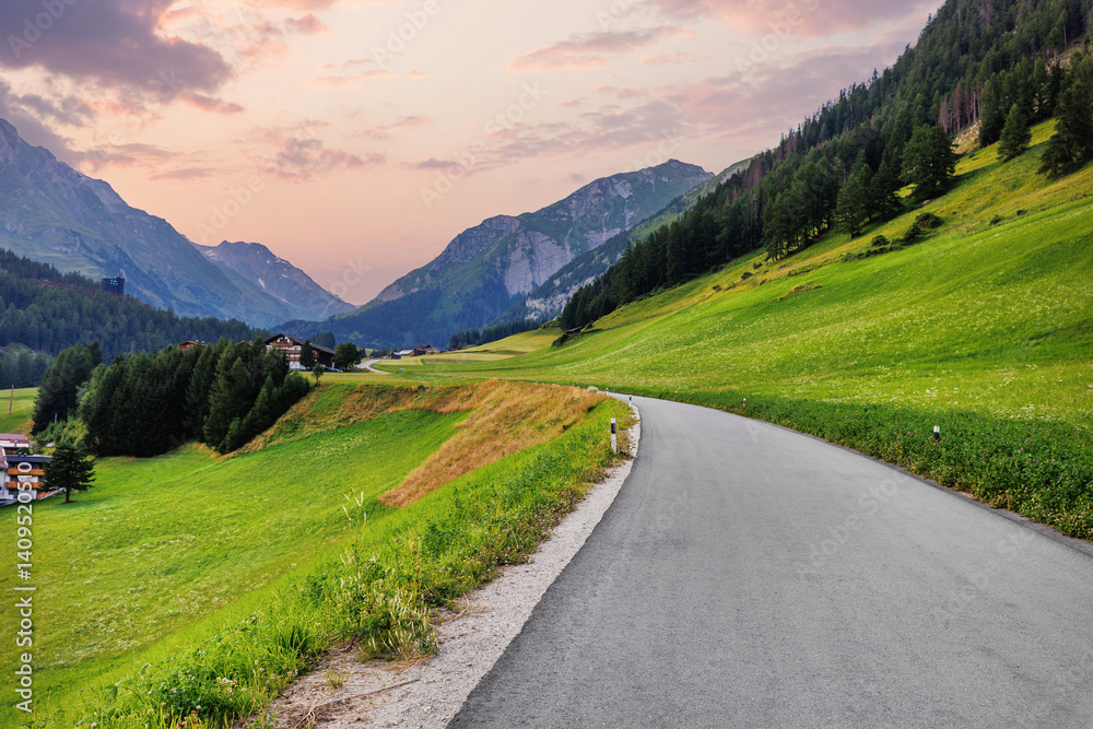 Scenic small countryside farm rural road green lush grass meadow mountain road alpine Austria sunset dramatic sky background. Panoramic Alps grassland forest pasture path. Family nature journey trip Scenic small countryside farm rural road green lush grass meadow mountain road alpine Austria sunset dramatic sky background. Panoramic Alps grassland forest pasture path. Family nature journey trip