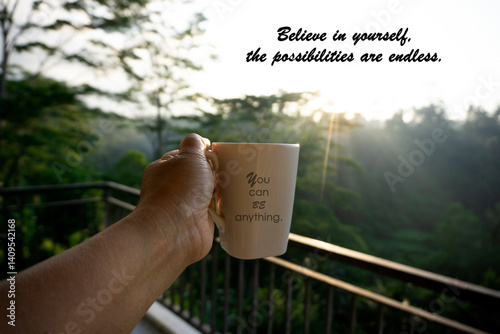 Motivation text on a cup in hand - You can be anything. And inspirational motivational quote - Believe in yourself, the possibilities are endless. On balcony with forest morning light view background.