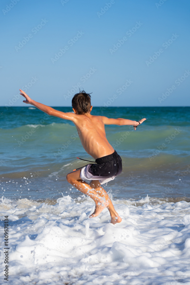 Fototapeta premium Boy jumping into ocean waves with outstretched arms, enjoying summer vacation