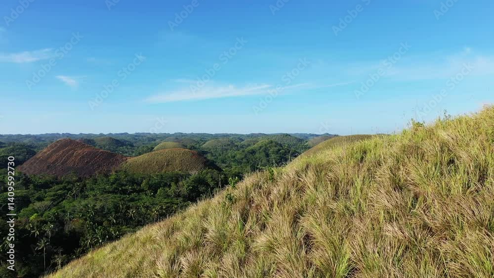 A mountain peak emerges from the Chocolate Hills amidst the green jungle and rice paddies, in Asia, Philippines, Bohol Island, near Panglao, in summer on a sunny day. A mountain peak emerges from the Chocolate Hills amidst the green jungle and rice paddies, in Asia, Philippines, Bohol Island, near Panglao, in summer on a sunny day.