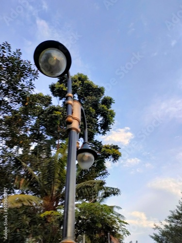 Low angle view of a street lamp against a bright, partly cloudy sky. Urban lighting fixture.