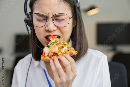 Asian businesswoman eating pizza while working with clients due to rush hour.