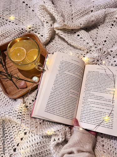 Cozy winter day at home in bed with warm knitted blanket, book and cup of tea. Leisure time on cold winter weekend. Christmas, relaxation and hygge concept