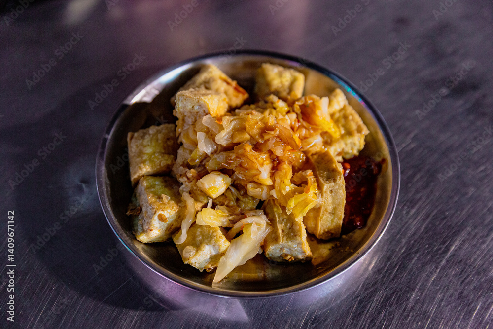 Close-up of Taiwanese fried stinky tofu with pickled cabbage and chili sauce in a round metal dish on a market table Close-up of Taiwanese fried stinky tofu with pickled cabbage and chili sauce in a round metal dish on a market table