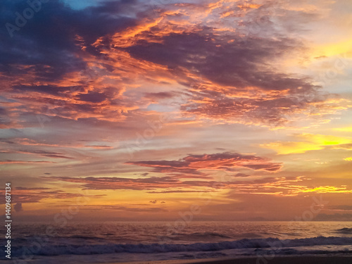 Obraz na płótnie Brilliant sun dips below the ocean horizon, painting the sky with vibrant yellow and orange hues. Its reflection shimmers on the gentle waves washing onto dark sand beach along the Costa Rican coast w salonie