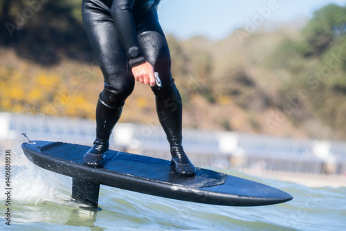 Obraz na plátně Close up of an man's legs standing on riding an electric powered hydrofoil trench board surfboard, in the the sea on a sunny day,  efoil, foil drive, hybrid foil assist