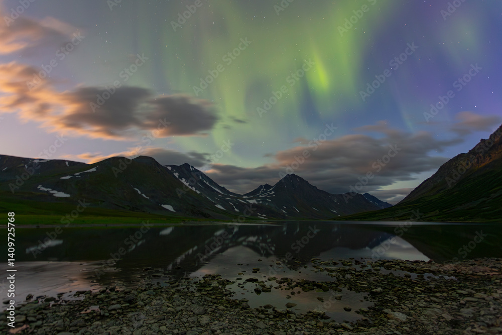 Aurora in the night sky cut the mountains, reflected in the water. Yamal. Russia