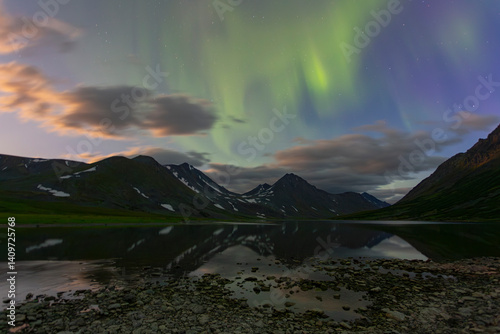 Aurora in the night sky cut the mountains, reflected in the water. Yamal. Russia