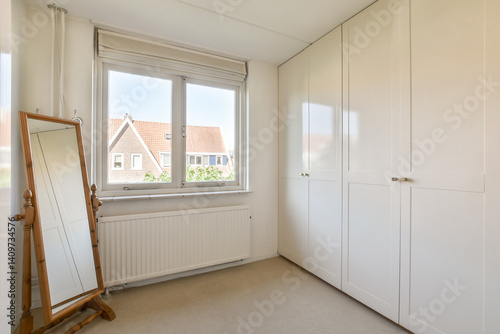 Фотография A bright and airy minimalist interior featuring a large mirror, built-in wardrobe, and ample natural light from the window