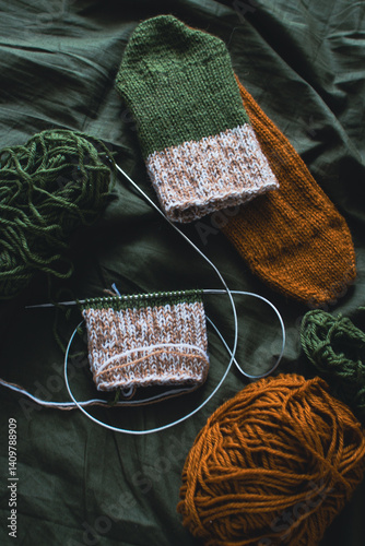 Obraz na płótnie Dark green and brown yarn ball with knitted socks and knitting needles. Wool threads with deep green background. Woven crochet close up. Knitting hobby. Knitwear concept. Needlework background. w salonie