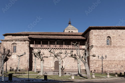 A large brick building with a large arched doorway. The building has a lot of windows and a large roof. The building is surrounded by trees and has a courtyard photo