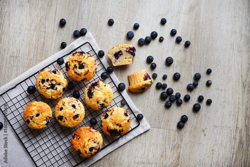 Vanilla muffins with blueberries on metal mesh tray and cotton towel near blueberries on grey background Vanilla muffins with blueberries on metal mesh tray and cotton towel near blueberries on grey background