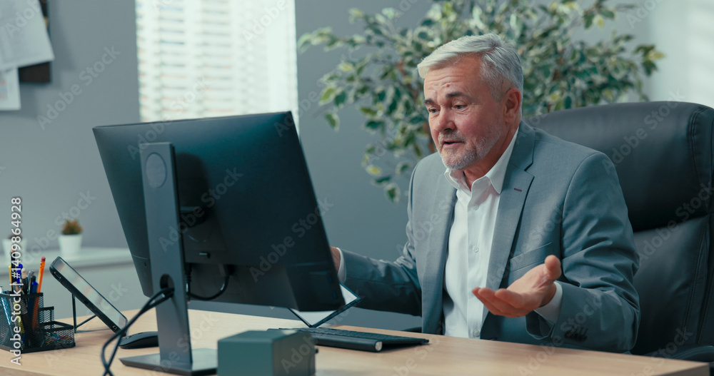 Head of the company, elderly man with gray hair, dressed in an elegant jacket, conducts a remote conference over the Internet, using video camera presenting documents asking questions spreading hands Head of the company, elderly man with gray hair, dressed in an elegant jacket, conducts a remote conference over the Internet, using video camera presenting documents asking questions spreading hands