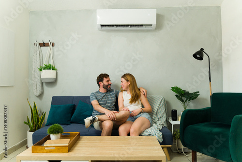 Happy couple relaxing on sofa under air conditioning unit at home