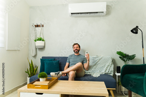 Obraz na płótnie Man relaxing on sofa using air conditioner remote control during summer heat w salonie