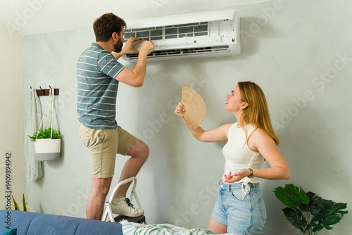 Obraz na płótnie Young couple fixing an air conditioning unit while woman holds hand fan w salonie