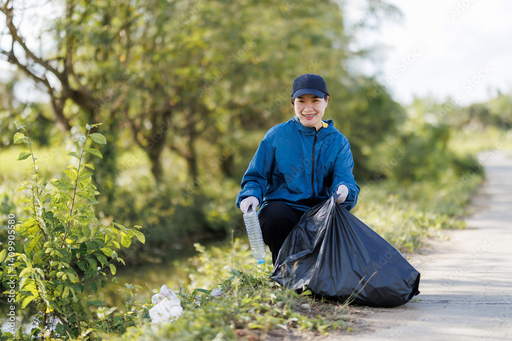 Fototapeta premium An Asian young woman volunteering to clean up trash along the canal.