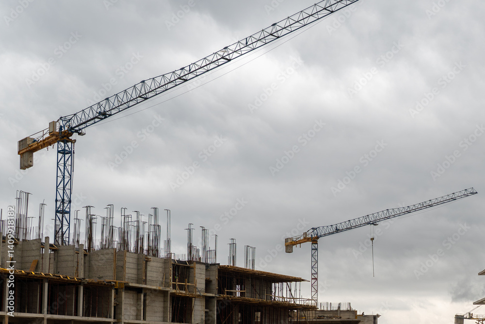 Modern construction site with two tower cranes and unfinished concrete building under dramatic cloudy sky. Image ideal for illustrating urban development, architecture, and infrastructure projects. Modern construction site with two tower cranes and unfinished concrete building under dramatic cloudy sky. Image ideal for illustrating urban development, architecture, and infrastructure projects.