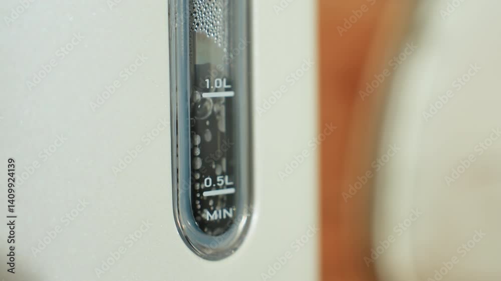 Close up of electric kettle water level indicator showing bubbles and steam rising inside during boiling process, highlighting transparent gauge markings in bright kitchen