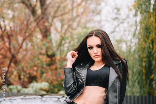 Confident woman in black leather jacket outdoors near car