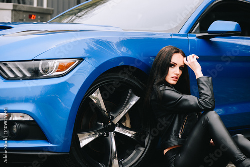 Woman posing on pavement next to blue Ford Mustang