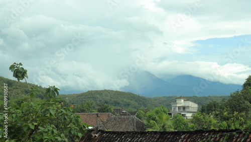 View of a village surrounded by lush green hills with misty mountains in the background, capturing the peaceful atmosphere and scenic beauty of rural landscapes