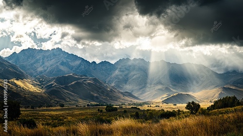Obraz na płótnie Wide-angle view of a mountain range with dramatic clouds and sunlight peeking through. w salonie