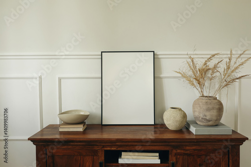 Elegant living room. Mahogany wooden cabinet dresser. Empty picture mock up poster frame. Clay vases, dry grass bouquet, ceramic bowl. Modern Scandinavian interior design, white wall background.
