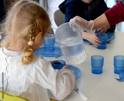 du personnel de cantine sert du pain ou de l'eau à de jeunes écoliers de maternelle ou de primaire