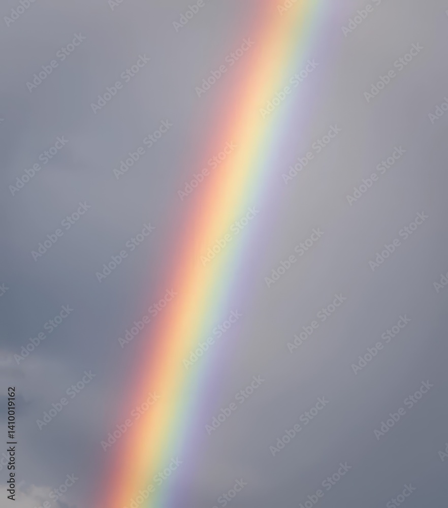 Vibrant rainbow arching across a cloudy gray sky, calming, rainbow