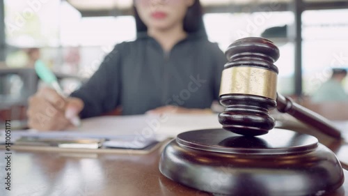 A woman is sitting at a desk with a gavel on it. She is writing something. There are two other people in the background