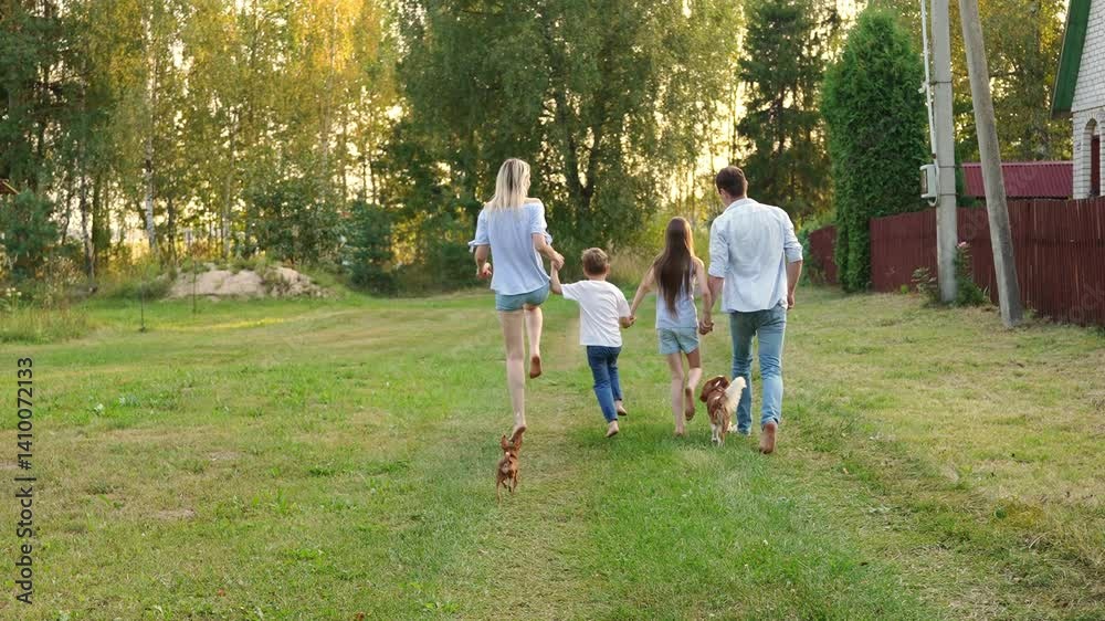 Family running barefoot holding hands on grass, view from behind, together with dog. Mom, dad, daughter and son enjoying country vacation, running and having fun together. Summer weekend concept Family running barefoot holding hands on grass, view from behind, together with dog. Mom, dad, daughter and son enjoying country vacation, running and having fun together. Summer weekend concept