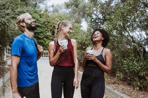 group of multiethnic friends drinking water or coffee and resting after doing exercise together in a City Park in Spain Europe. Hispanic man and afro hair woman wearing athletic clothing