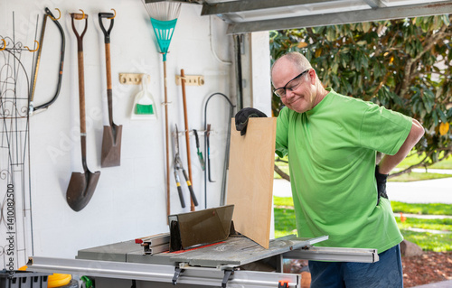 Senior man experiences backache while woodworking in a garage during hobby time. - series