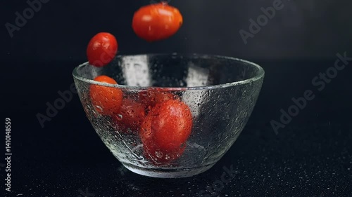 Fresh cherry tomatoes falling into wet glass black background. Eating healthy raw organic food, vitamins, vegetables concept. Slow motion