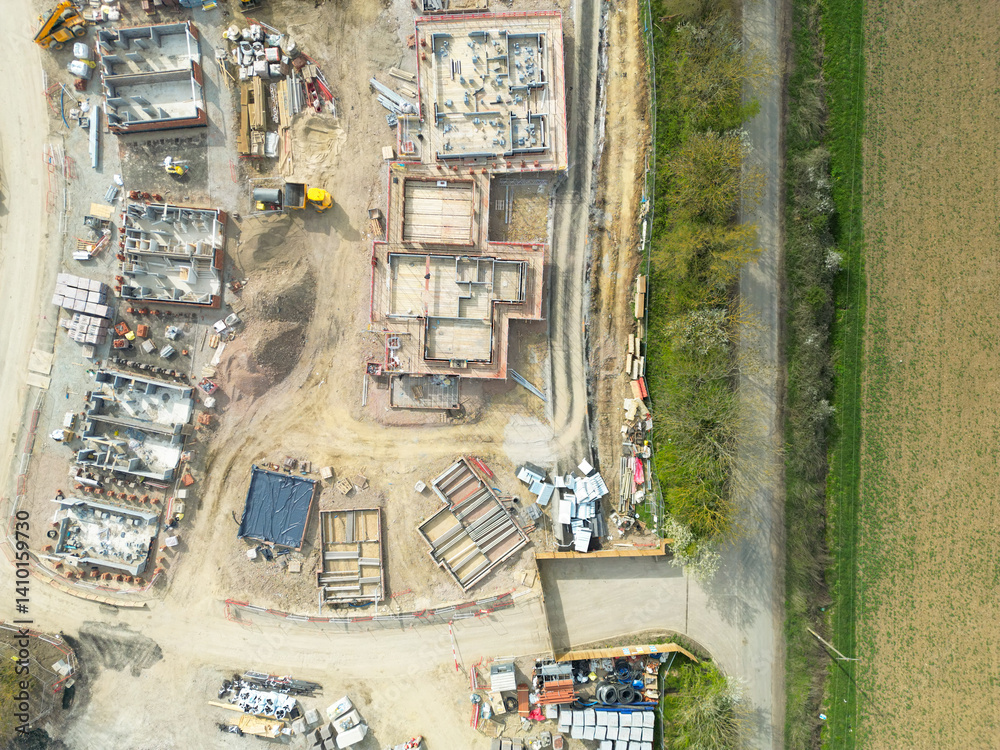 Drone high altitude view of new foundations and house footings seen on a housing development site in rural England. Seen adjacent to a farm field.