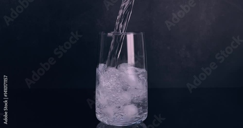 Carbonated mineral water flowing into a glass with ice cubes on black background. Healthy and fresh water. Slow motion