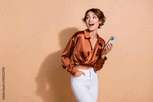 Photo of adorable excited girl wear brown blouse communicating modern gadget looking empty space isolated beige color background