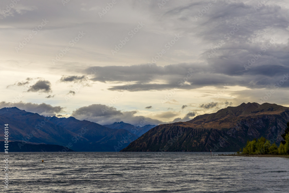 Lake Wanaka, a summer cloudy afternoon with a mountain range and the town of Wanaka on the shore. South Island, New Zealand